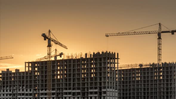 Construction site with cranes and buildings at orane yellow sunset.