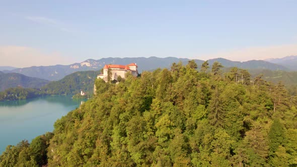 Smooth cinematic dolly in aerial to reveal Bled Castle overlooking Lake Bled high in the Julian Alps