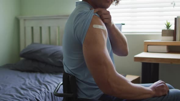 Midsection of caucasian disabled man in wheelchair showing bandage on arm after covid vaccination