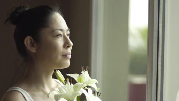 Woman holding fresh lilies and looking out window, then turning to smile at camera