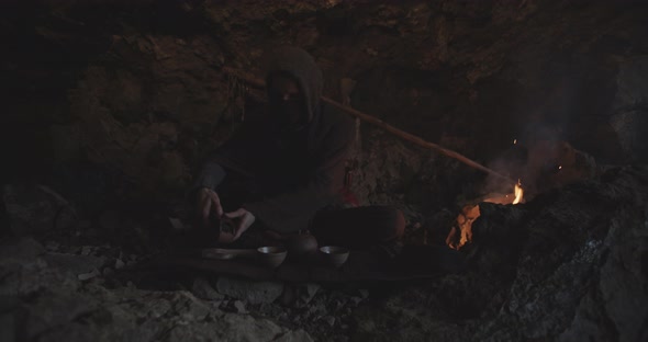 Hooded Figure Preparing Tea In Cave