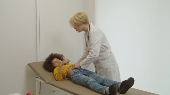 Caring Female Pediatrician Examining Abdomen of Sick Preschool Age Multiracial Boy in Medical Office