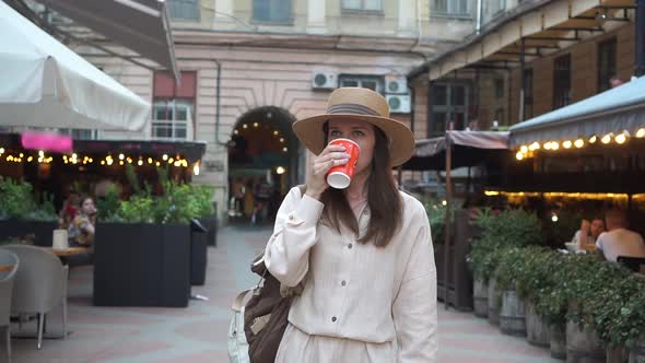 Happy Attractive Woman Wearing Hat Drinking Coffee and Looking Around While Walking on the Old City