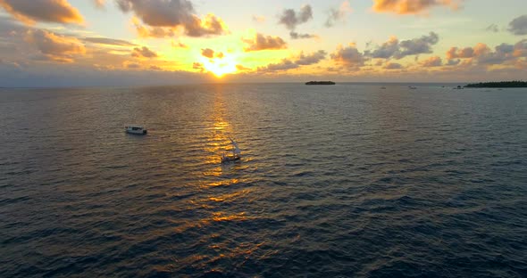 Aerial drone view of a man and woman sailing on a boat to a tropical island at sunset.