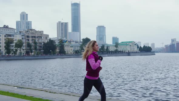 Beautiful Blonde Girl Runs Along Urban Embankment