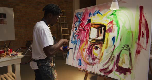 African american male artist wearing apron painting with palette knife on canvas at art studio