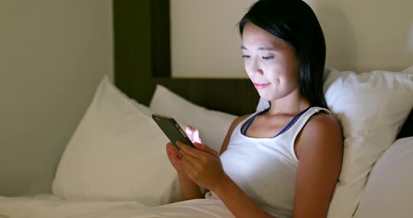 Woman use of mobile phone and lying on bed at night 