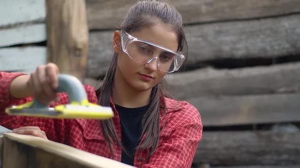 The girl with glasses works. Carpenter grinds the boards of the box