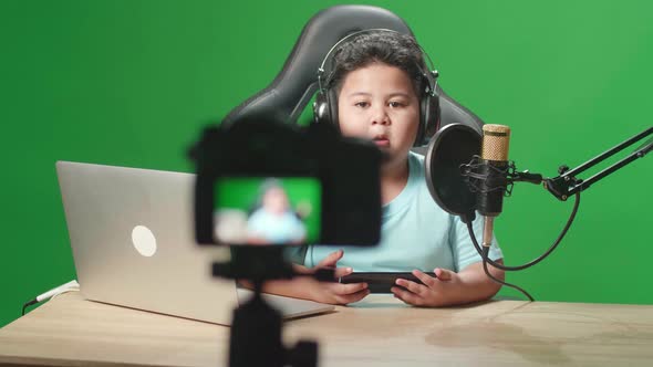 Asian Little Boy Holding Mobile Phone And Talking To Camera While Live Stream On Green Screen