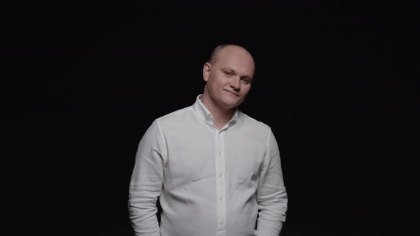 An elegant bald man in a white shirt stares at the camera and smiles