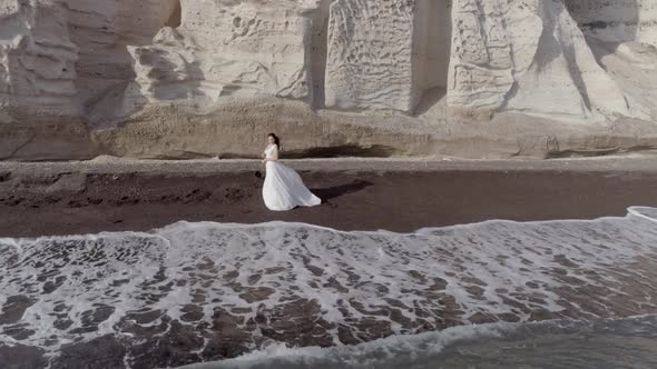 Aerial view of woman with wedding dress on beach Santorini island, Greece.