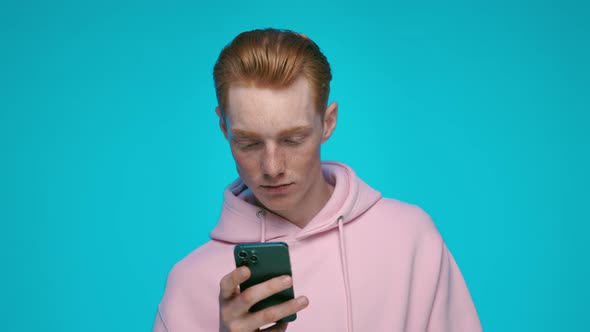 Redhead Male Hipster in Pink Hoodie Using Modern Smartphone