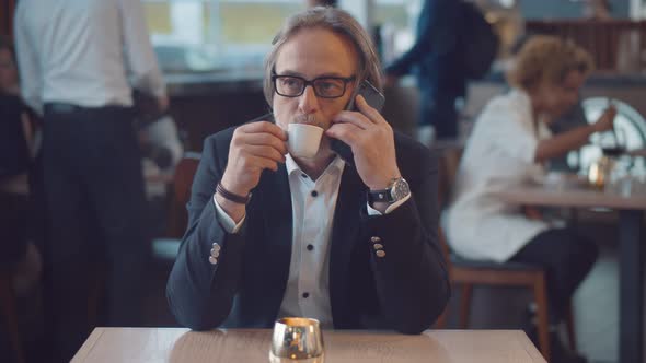 Senior Businessman on Coffee Break in Restaurant Having Phone Conversation with Business Partner