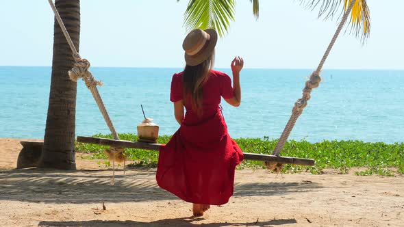 Travel Woman in Summer Dress Sit on Swing at Tropical Beach By Turquoise Sea