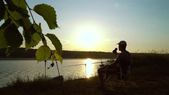 Silhouette of Fisherman on River Bank Drinking Alcohol at Sunset