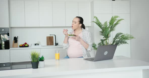 Expectant Woman Eats Salad Watching Video in Kitchen