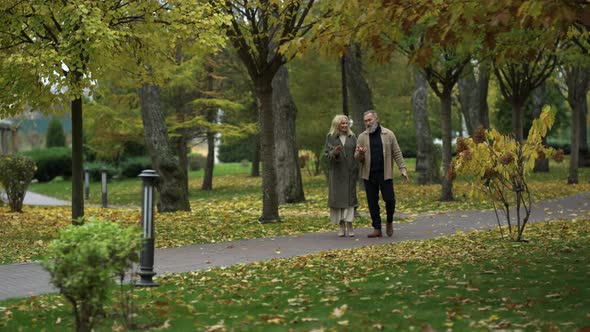 Wide Shot of Happy Elderly Couple Walking Along Path in Elegant Outerwear