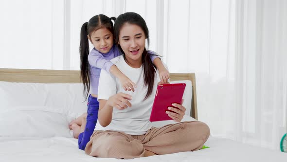 Happy mum and her daughter having fun talking using learning digital tablet at home