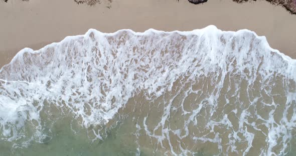 Static top down view of tropical beach, foamy ocean waves washing sand. Waves hitting sand beach