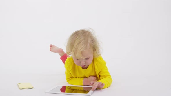 Adorable Focused Toddler Girl Lying on Floor Playing Apps on Smartphone Tablet
