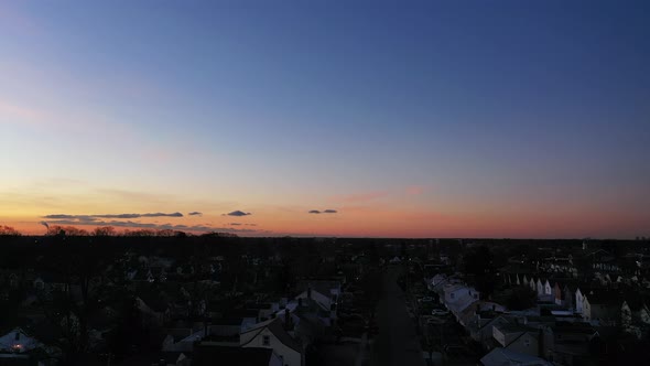 An aerial shot over a suburban neighborhood during a golden sunrise. The camera dolly in & boom up t