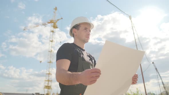 A Man in a Helmet Is Holding a Construction Plan in His Hands. A Builder Is Checking Blueprints