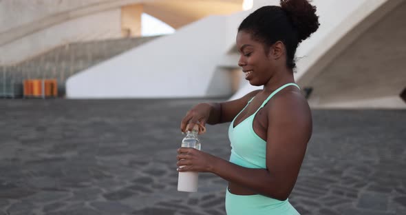 Happy african girl drinking water after sport workout