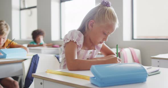 Video of focused caucasian girl sitting at desk in classsroom