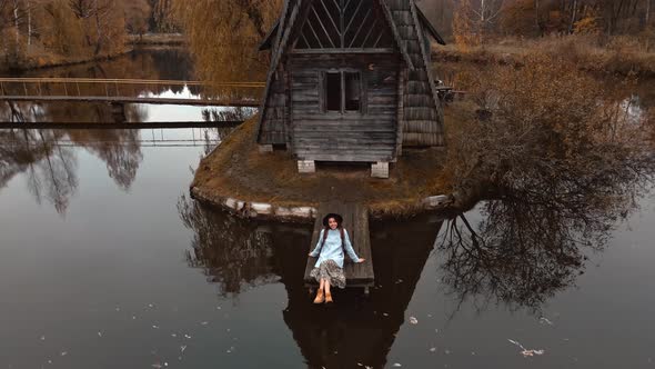 Aerial View of Girl Traveler Standing By Old Wooden House Chalet By Lake Among Trees at Forest with