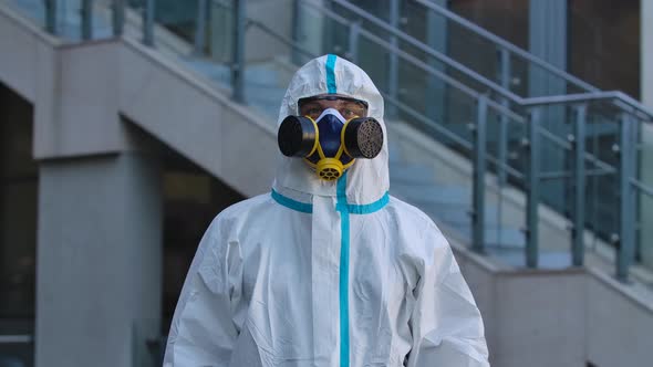 Portrait of a Young Man in a Protective Suit, Respirator, Gloves and Safety Glasses Looks at the