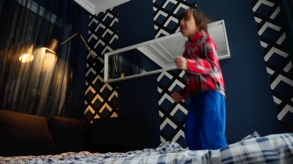 Dark Haired Boy in a Plaid Shirt Jumps on the Bed Home