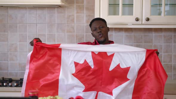 Front View Positive African American Man Shacking Canadian Flag Posing in Kitchen Indoors