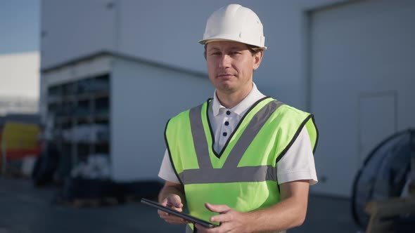 Happy Caucasian Adult Man Closing Tablet Looking at Camera Smiling Posing at Manufacturing Plant