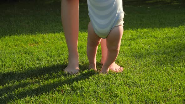 Closeup of Barefoot Baby Boy and Mother Standing on Fresh Green Grass at Park