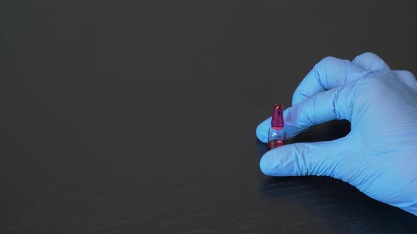 Hand in blue medical protective glove holds ampoule with vaccine for treatment from virus epidemic