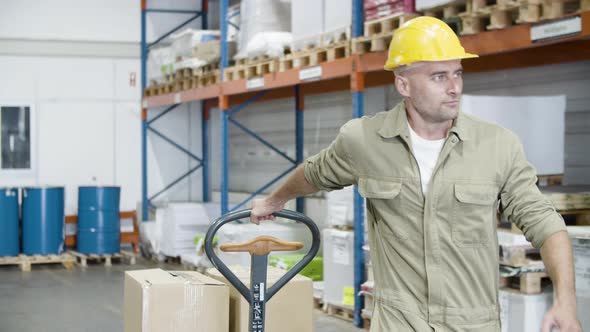 Serious Male Worker Pulling Trolley with Cardboard Boxes