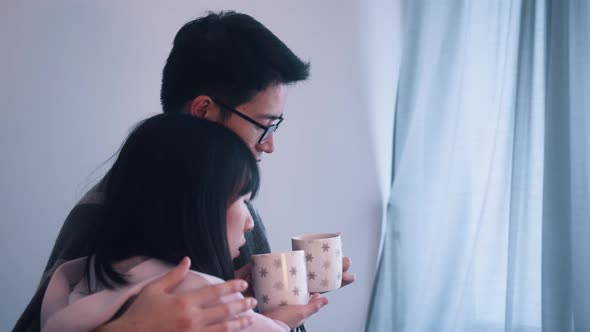 Young Couple Hugging Near the Window with Hot Tea on Stormy Day