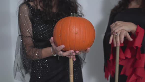 Women In Witch Costume Holding Broomstick And Pumpkin During Halloween