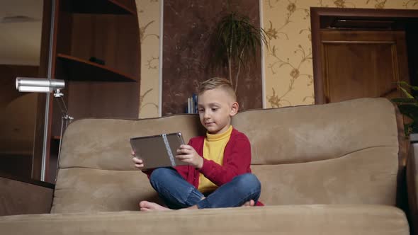 Boy Relaxing on Comfortable Sofa in Contemporary Living-Room and Playing Online Video Game