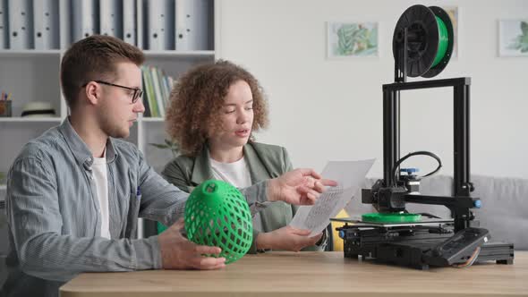 Creative Man and Woman Use Modern Technology and Hold a 3D Model in Their Hands While a 3D Printer