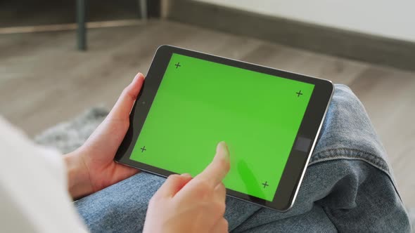 Woman holding in hands a digital tablet with green screen for internet online.