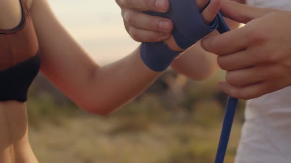 Closeup of the athlete's hands and her trainer, who ties her hands with boxing bandage before traini