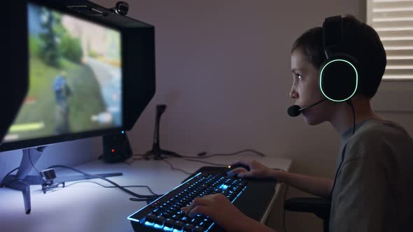 Young boy sitting in front of a computer, playing a game wearing a headset