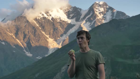 Man Bites Apple and Enjoys Fruit Taste Standing Against Hill