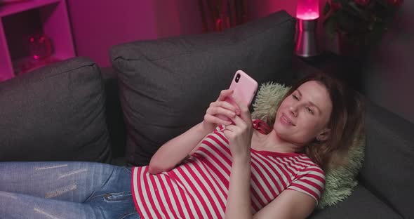 Girl Holding Smart Phone Using Mobile Apps Watching Funny Video Laughing Lying on Couch