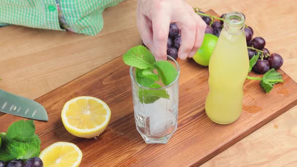 Process of making lemonade drink at the kitchen, glass with ice cubes, lemon slices and mint