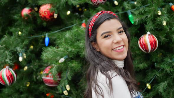 A gorgeous hispanic woman smiling and looking merry celebrating Christmas with a tree and festive ho