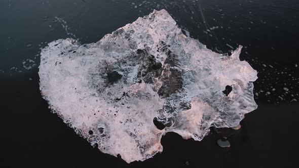 Top down close up view of small piece of ice on black sand Diamond Beach, Iceland. Sunset.