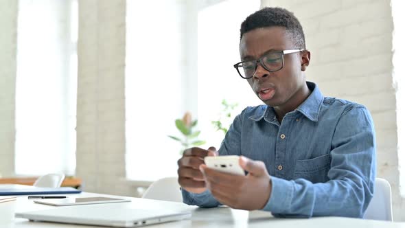 Upset Young African Man Reacting to Loss on Smartphone in Office