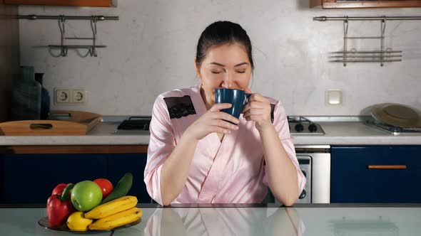 Woman Sits at Table and Sniffs Coffee Smell Holding Cup